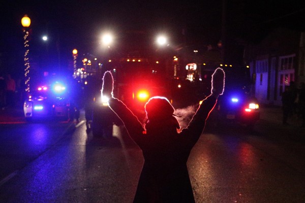 A protester raises her hands in the street as police use tear gas to try to take control of the scene near a Ferguson Police Department squad car after protesters lit it on fire on Tuesday, Nov. 25, 2014, in the wake of the grand jury decision not to indict officer Darren Wilson in the shooting death of Ferguson, Mo., teen Michael Brown. (Anthony Souffle / Chicago Tribune/TNS)
